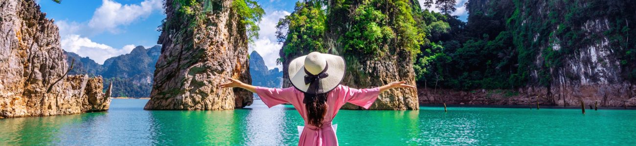 Beautiful girl standing on the boat and looking to mountains in Ratchaprapha Dam at Khao Sok National Park, Surat Thani Province, Thailand.